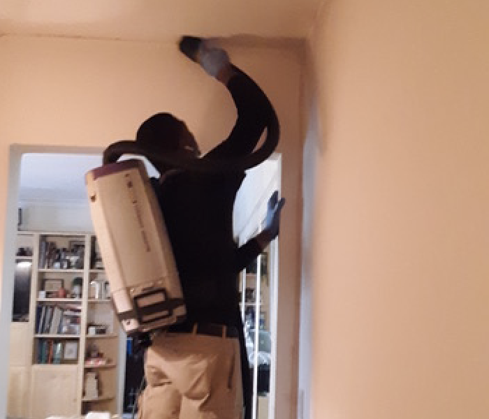 SERVPRO team member standing on a stool cleaning walls and ceiling.