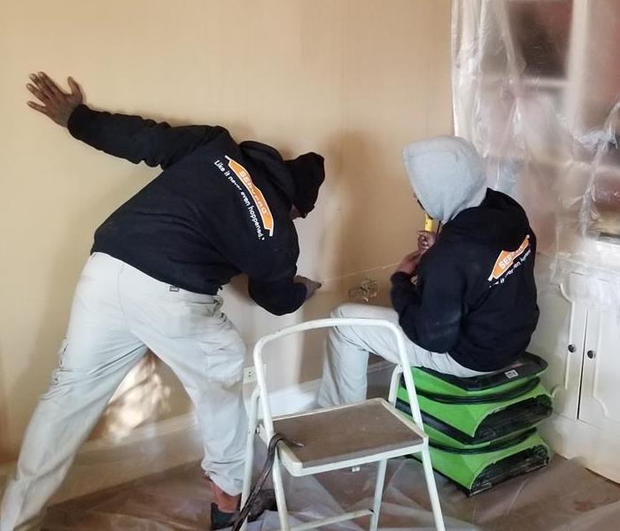 two people assessing the wall in a home to begin restoration