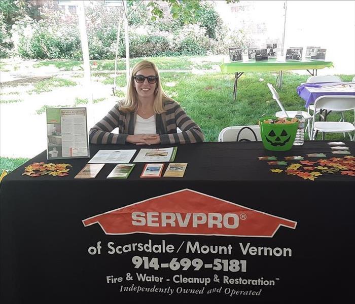 a woman sitting at an outdoor booth with SERVPRO logo on the tablecloth