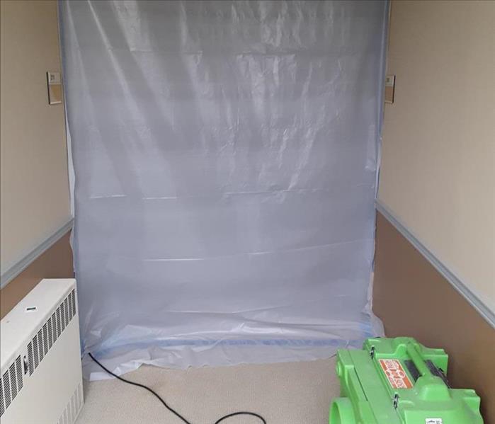 Tarp taped up on walls and air mover on the floor